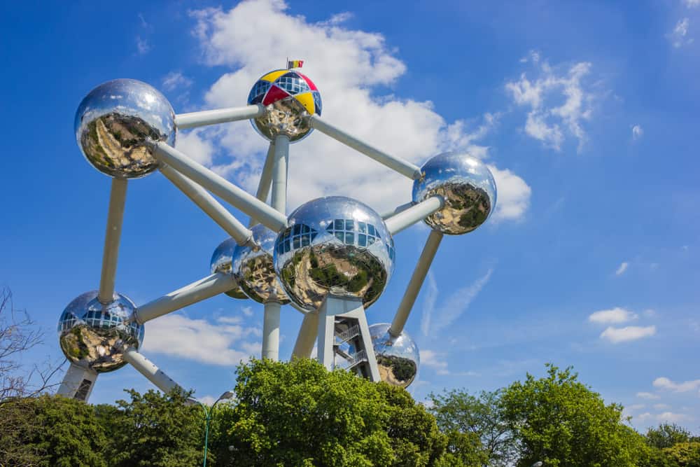 Den store stålkonstruktion Atomium med træer i forgrunden og blå himmel i baggrunden.