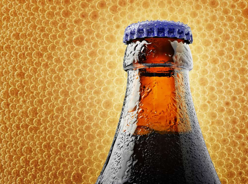 Toppen af en flaske belgisk Belgisk Chimay øl med bobler i baggrunden.