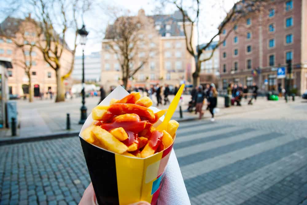 Belgiske pommes fritter i forgrunden og gadeliv i baggrunden.