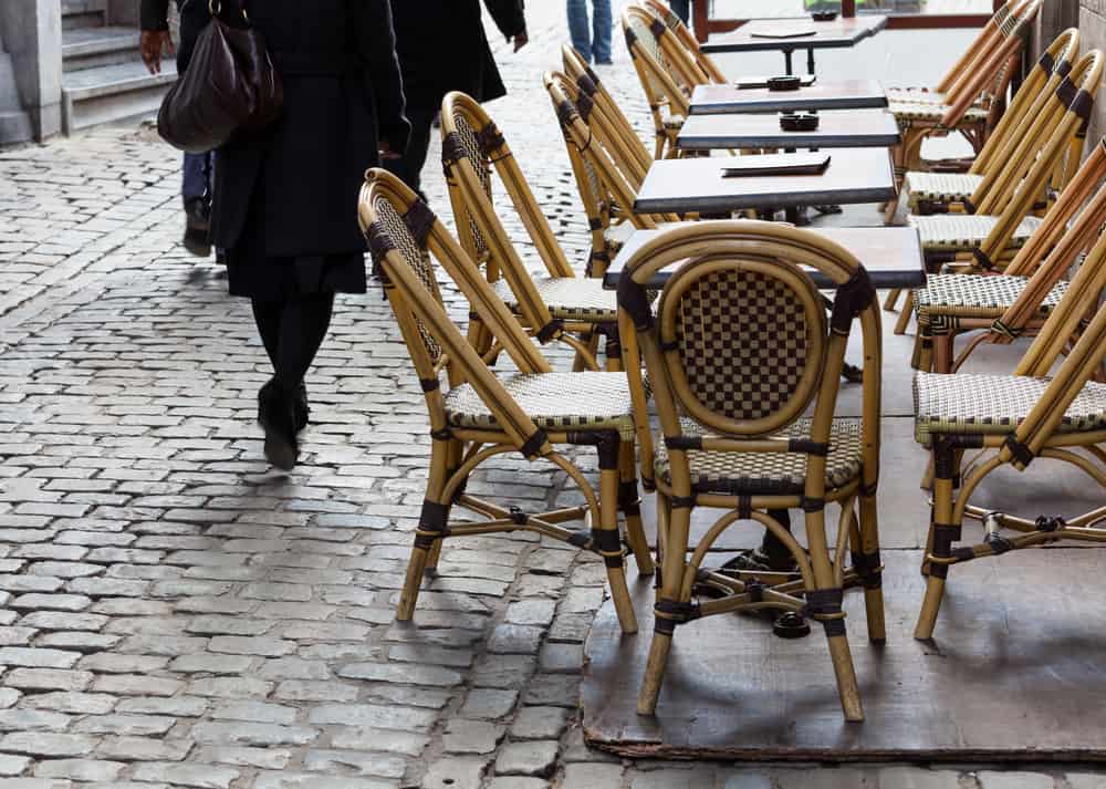 Caféborde- og stole ved brostensbelagt gade i Bruxelles. Gående personer i baggrunden.