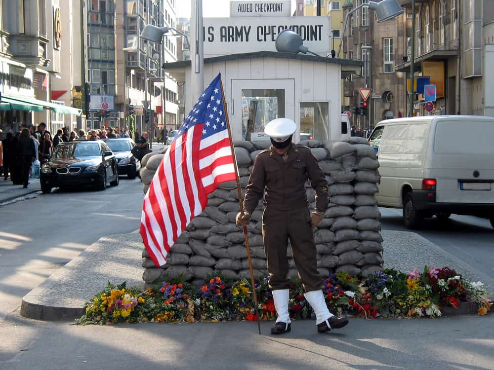 Soldat med amerikansk flag ved Checkpoint Charlie i Berlin
