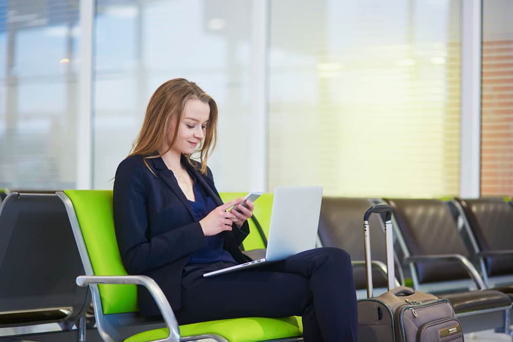 Ung kvinde som arbejder på computer og telefonen i lufthavnen.