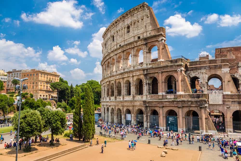 Colosseum i Rom i Italien set udefra. En flot lys himmel og mange turister på gaden.