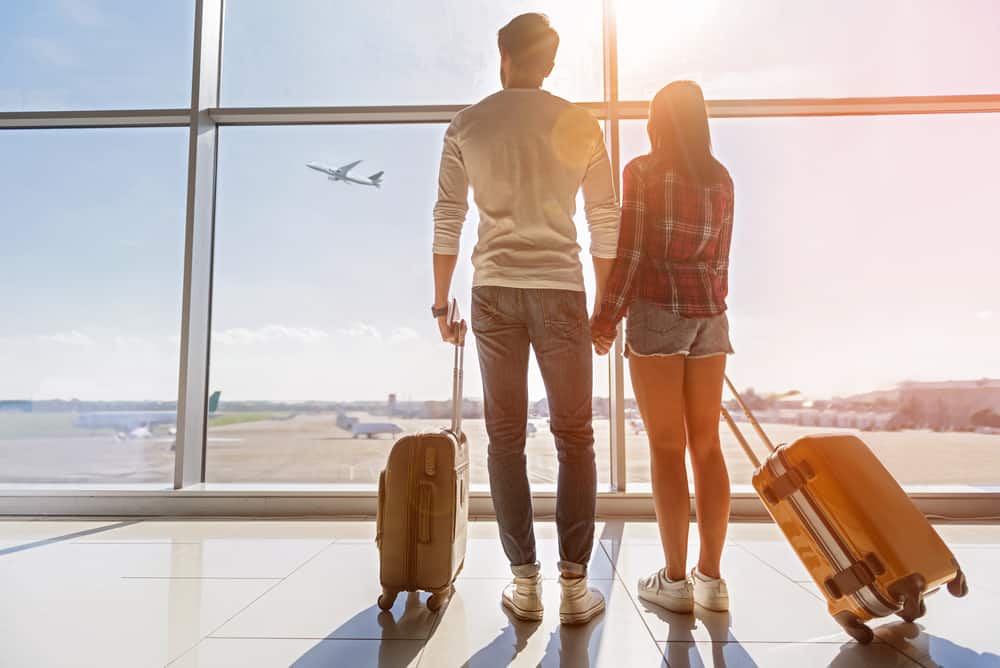 Et par der står i en lufthavn med deres kufferter.